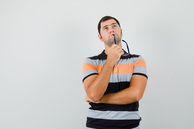 Jonge man in t-shirt opzoeken terwijl hij zijn bril bijt en nadenkend ruimte voor tekst zoekt