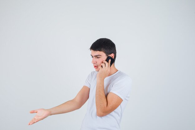 Jonge man in t-shirt praten op mobiele telefoon en kijken opgewonden, vooraanzicht.