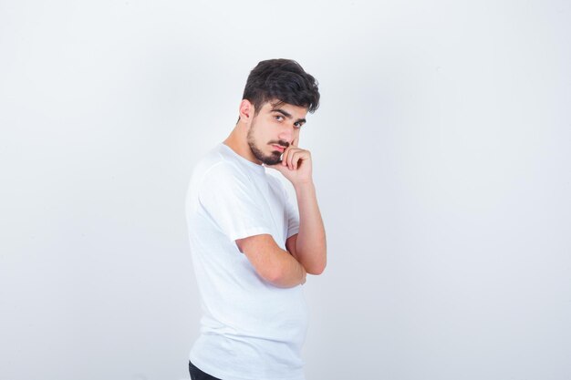 Jonge man in t-shirt staat in denkende pose en kijkt aarzelend looking
