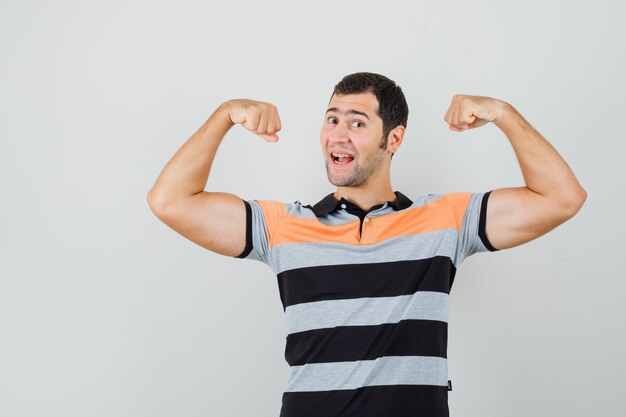 Jonge man in t-shirt toont zijn armspieren en kijkt flexibel