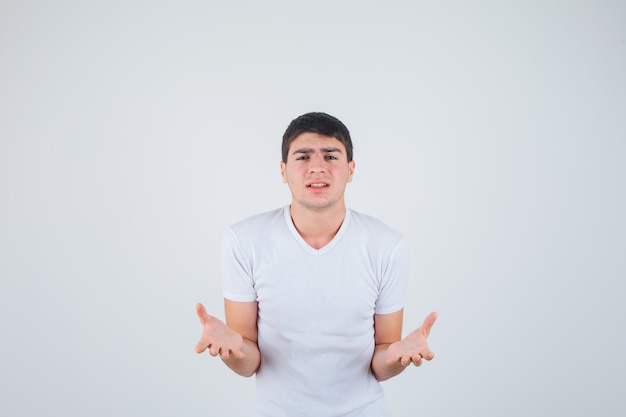 Jonge man in t-shirt uitrekken hand in vragend gebaar en op zoek opgewonden, vooraanzicht.