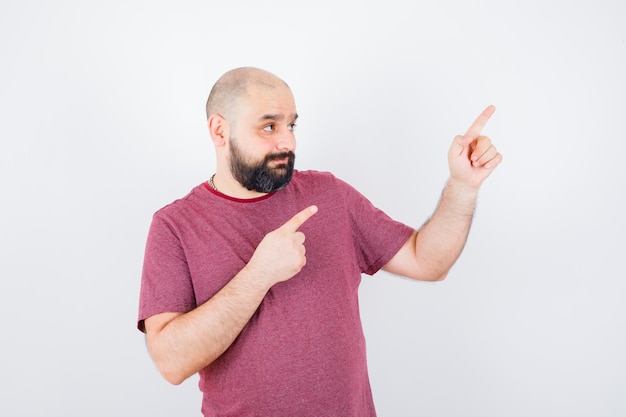 Jonge man in t-shirt wijzend naar de rechterbovenhoek en zelfverzekerd, vooraanzicht.