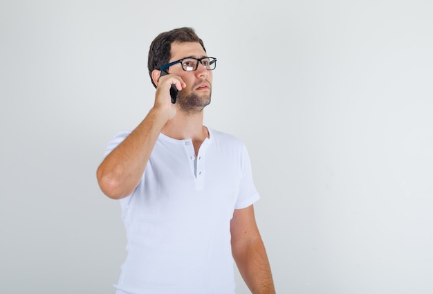 Jonge man in wit t-shirt, bril praten op mobiele telefoon en op zoek attent