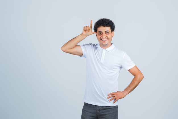 Jonge man in wit t-shirt, broek die een pistoolgebaar toont en er gelukkig uitziet, vooraanzicht.