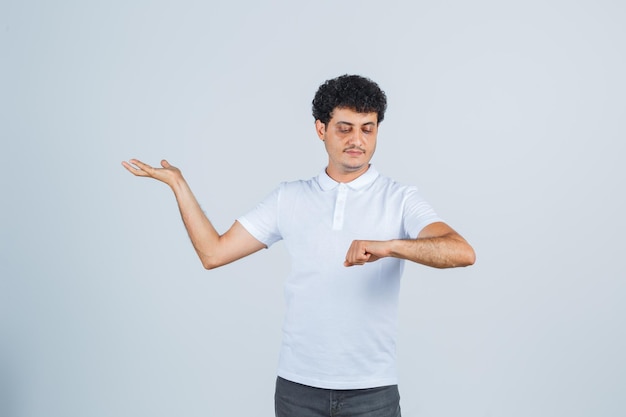 Jonge man in wit t-shirt, broek kijkend naar horloge deed alsof hij gedragen was en zag er zelfverzekerd uit, vooraanzicht.