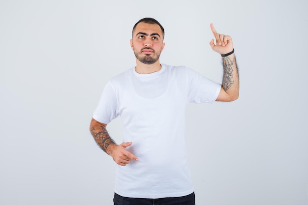 Jonge man in wit t-shirt en zwarte broek die wijsvinger opheft in eureka-gebaar en peinzend kijkt