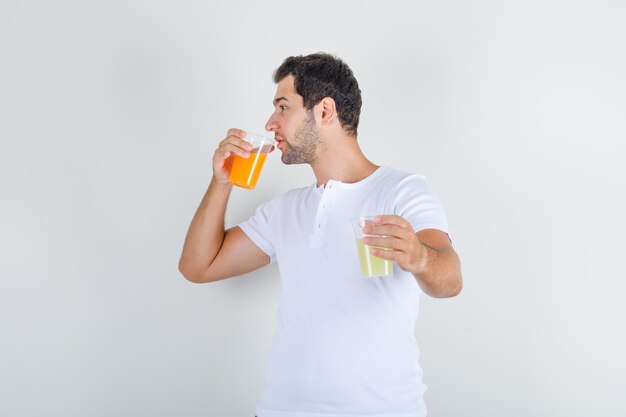 Jonge man in wit t-shirt glas sap drinken en dorstig kijken