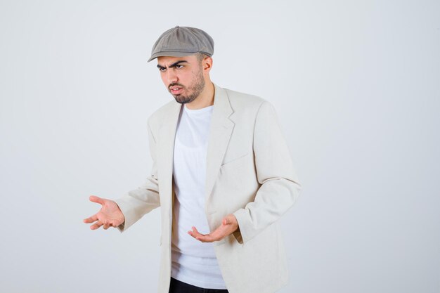 Jonge man in wit t-shirt, jasje en grijze pet die één hand uitrekt als iets vast te houden en er serieus uitziet