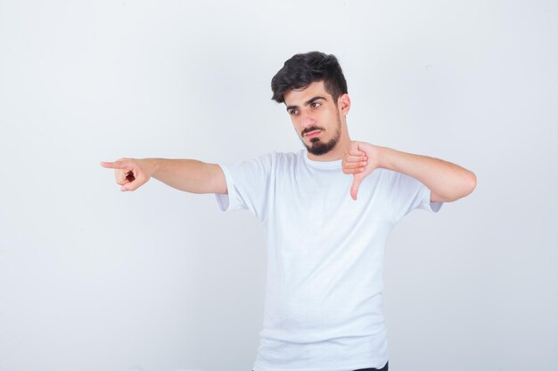 Jonge man in wit t-shirt met duim naar beneden, wegwijzend en zelfverzekerd kijkend