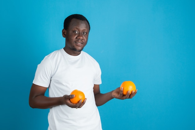 Jonge man in wit t-shirt met twee zoete oranje vruchten tegen blauwe muur