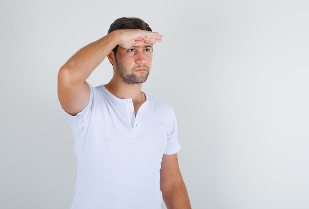 Jonge man in wit t-shirt Vooruitblikkend met de hand op het voorhoofd