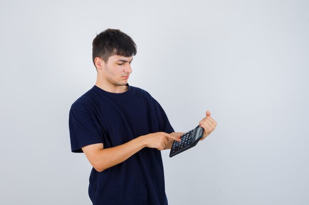 Jonge man in zwart t-shirt berekeningen maken op de rekenmachine en op zoek naar druk, vooraanzicht.