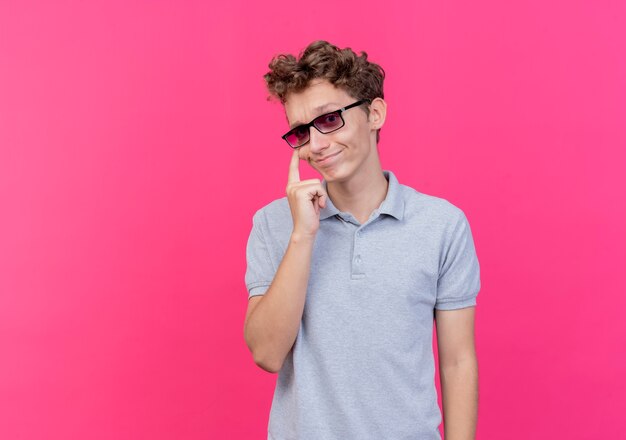 Jonge man in zwarte bril met grijs poloshirt wijst met zijn oog lachend naar je gebaar over roze