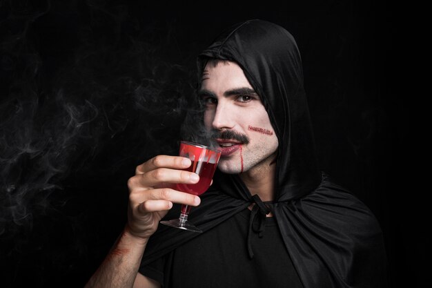 Jonge man in zwarte mantel met witte gezicht drinken stomen rode vloeistof