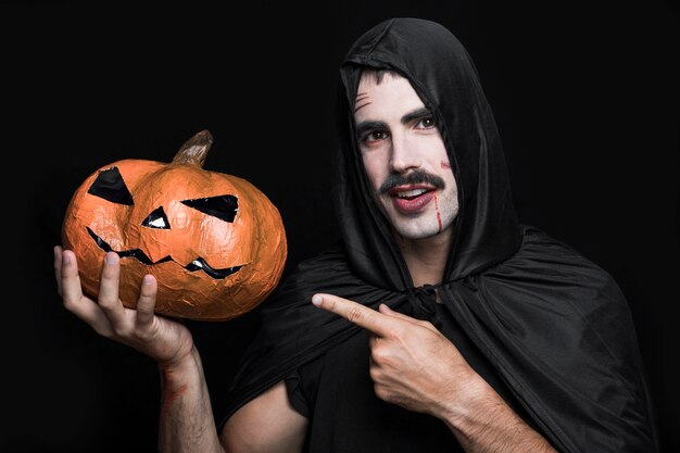 Jonge man in zwarte mantel wijzend op Halloween-pompoen