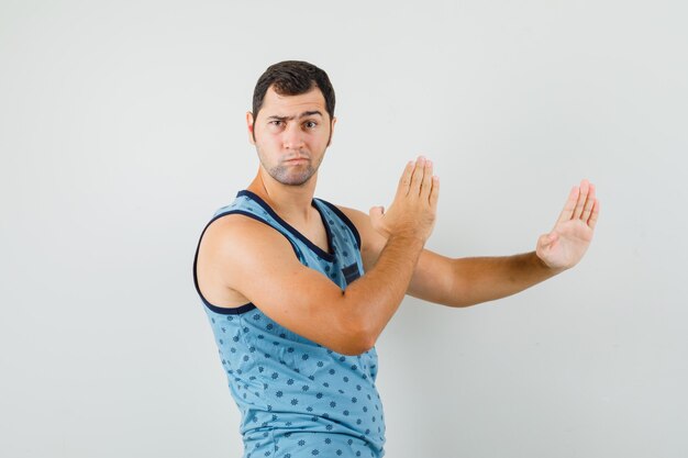 Jonge man karate hakken gebaar in blauwe hemd tonen en op zoek strikt. vooraanzicht.