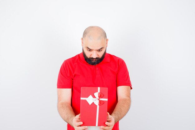 Jonge man kijken naar geschenkdoos in rood shirt vooraanzicht.