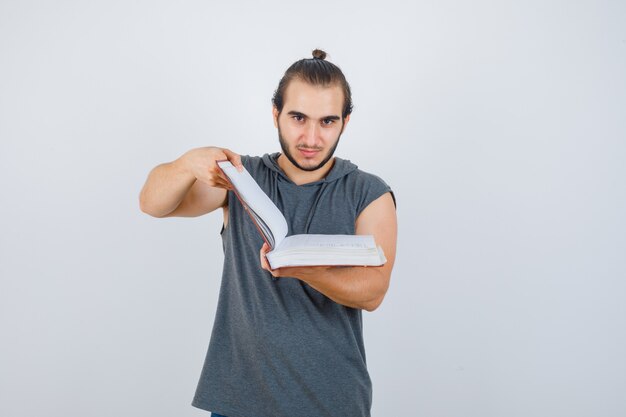 Jonge man kijkt door boek in mouwloze hoodie en ziet er zelfverzekerd uit. vooraanzicht.