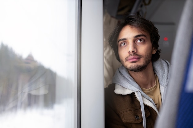 Jonge man kijkt door het raam naar buiten terwijl hij met de trein reist