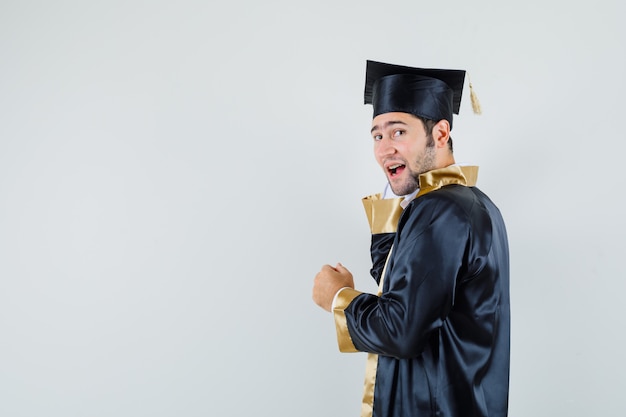 Jonge man kijkt naar camera in afgestudeerde uniform en ziet er knap uit.​