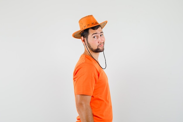 Jonge man kijkt naar camera in oranje t-shirt, hoed en kijkt zelfverzekerd.