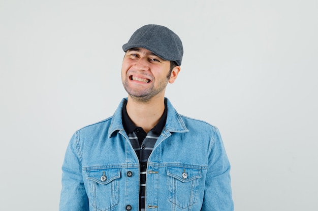 Jonge man kijkt naar camera in pet, t-shirt, jasje en kijkt vrolijk