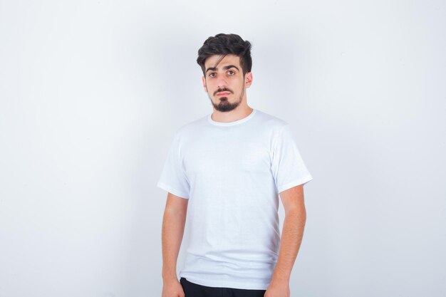 Jonge man kijkt naar camera in wit t-shirt en ziet er elegant uit