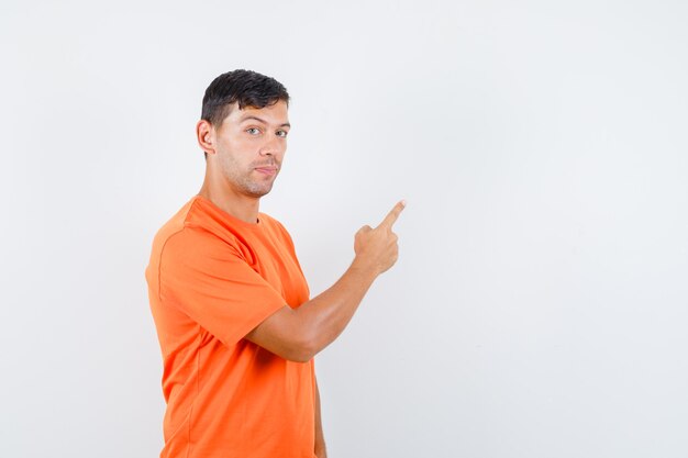 Jonge man kijkt naar de camera terwijl hij weg wijst in oranje t-shirt en kijkt positief