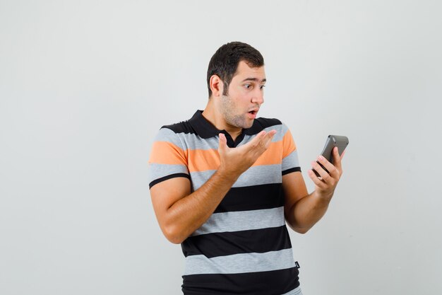 Jonge man kijkt naar iets op de telefoon in t-shirt en kijkt stomverbaasd