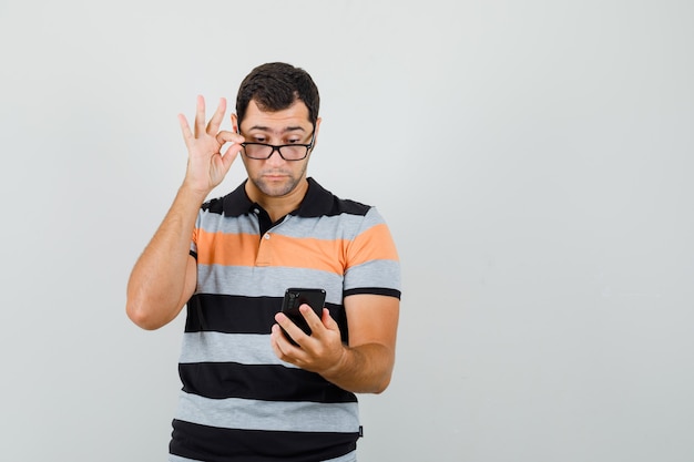 Jonge man kijkt naar telefoon in t-shirt, bril en kijkt gericht. ruimte voor tekst