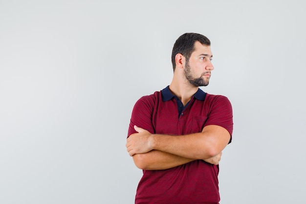 Jonge man kijkt opzij in rood t-shirt en kijkt serieus, vooraanzicht.