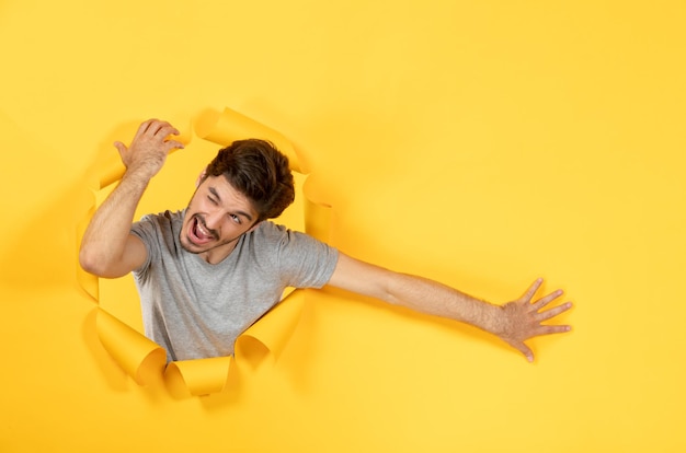 Jonge man kijkt uit gescheurd geel papier oppervlak