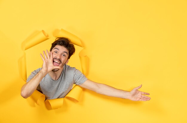 Jonge man kijkt uit gescheurd geel papier oppervlak