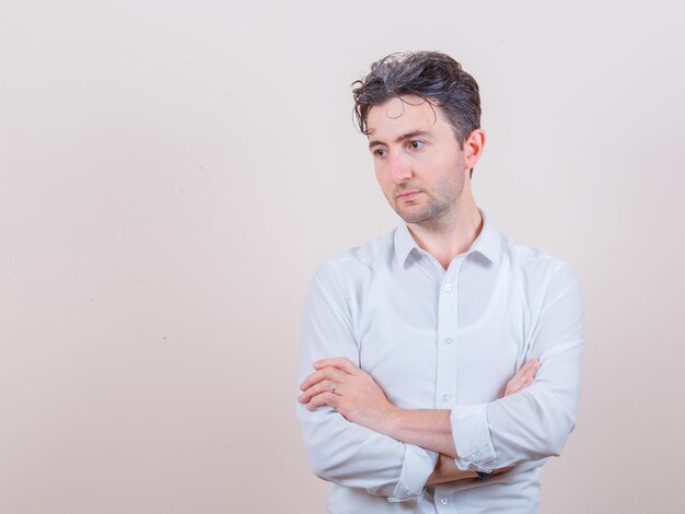 Jonge man kijkt weg met gekruiste armen in wit overhemd en kijkt bedachtzaam