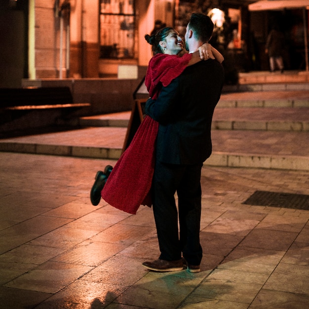 Jonge man knuffelen opknoping lachende vrouw op straat in de avond