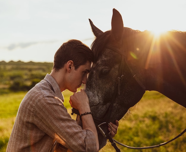 Jonge man knuffelt een paard in een veld onder het zonlicht in de avond