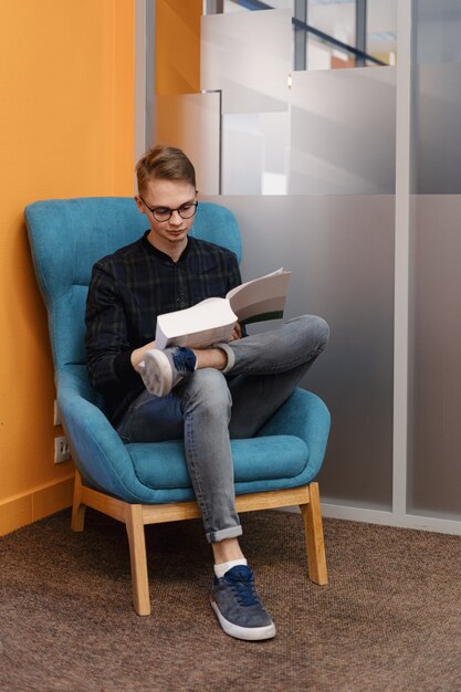 Jonge man leest een dik boek in een fauteuil