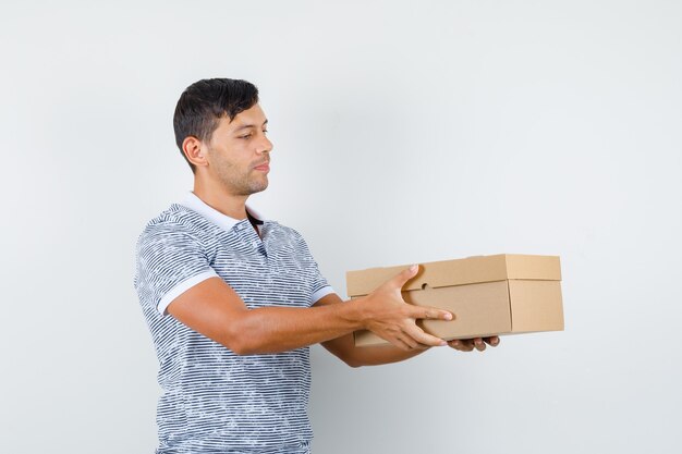 Jonge man levert kartonnen doos in t-shirt en kijkt verantwoordelijk