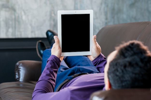 Jonge man liggend op de bank kijken naar digitale tablet met zwart scherm