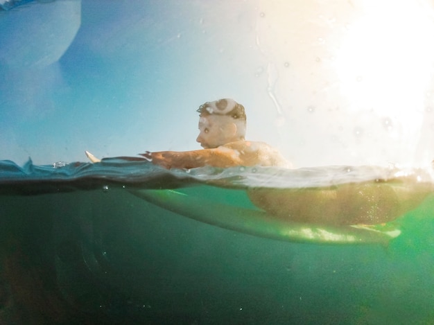 Jonge man liggend op surfplank in water