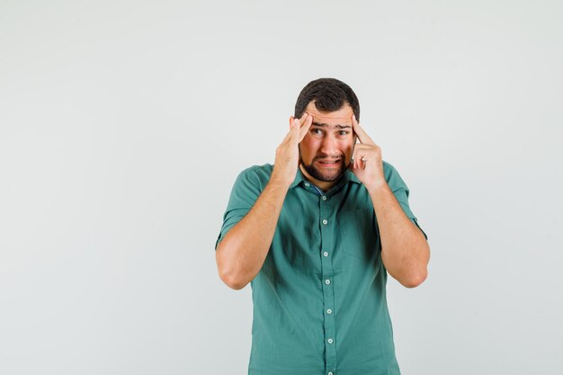 Jonge man lijdt aan hoofdpijn in groen shirt en ziet er ongemakkelijk uit, vooraanzicht.