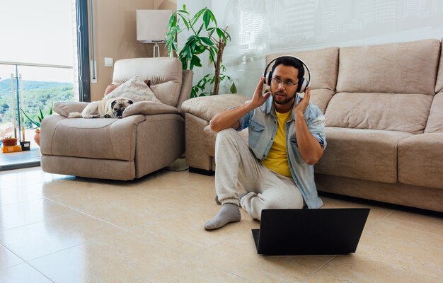 Jonge man, luisteren naar muziek met een koptelefoon en met behulp van een laptop om vanuit huis te werken