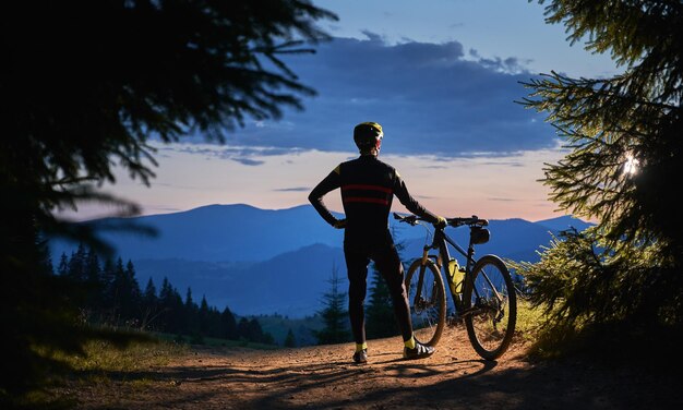 Jonge man met een fiets genieten van zonsondergang in de bergen