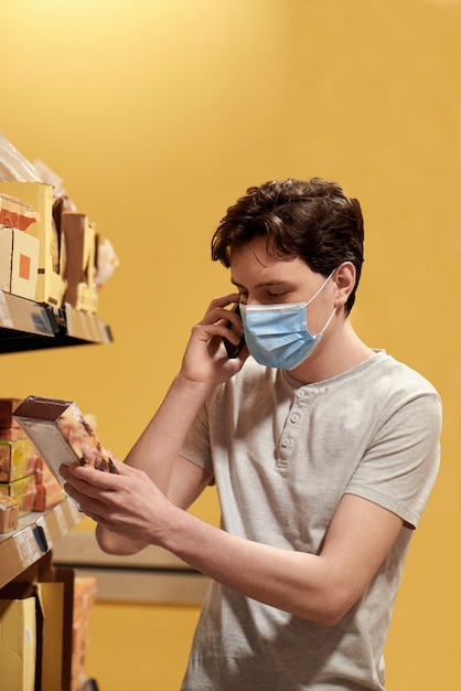 Jonge man met een gezichtsmasker kijken naar snacks in een supermarkt