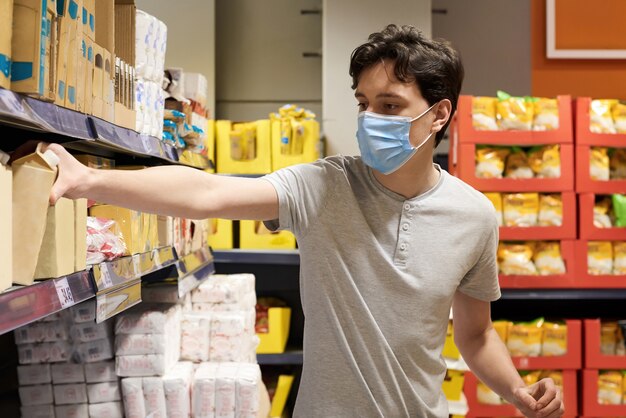 Jonge man met een gezichtsmasker kijken naar snacks in een supermarkt