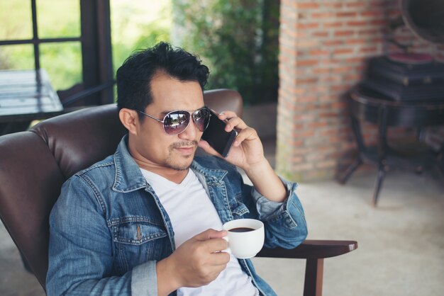 Jonge man met een smartphone lacht ontspannen bij cafe.