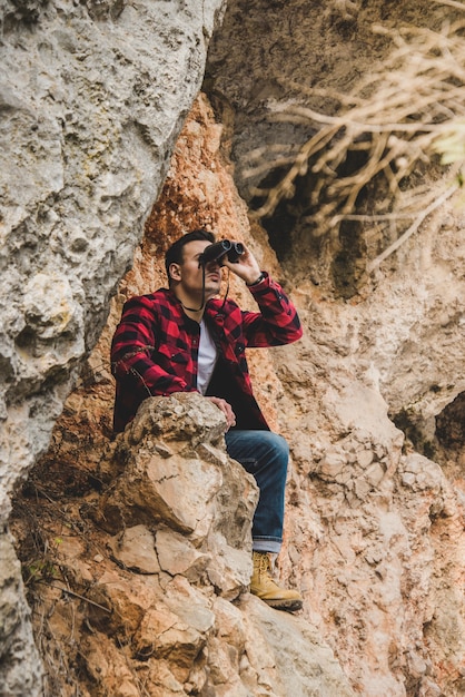 Jonge man met een verrekijker die op een rots zit