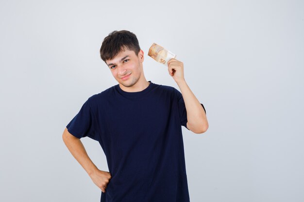 Jonge man met eurobiljet in zwart t-shirt en op zoek zelfverzekerd. vooraanzicht.