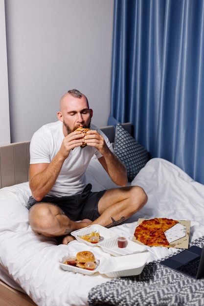 Jonge man met fast food thuis in de slaapkamer op bed