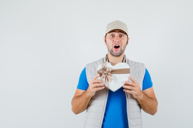 Jonge man met geschenkdoos in t-shirt, jas en op zoek gelukkig, vooraanzicht.